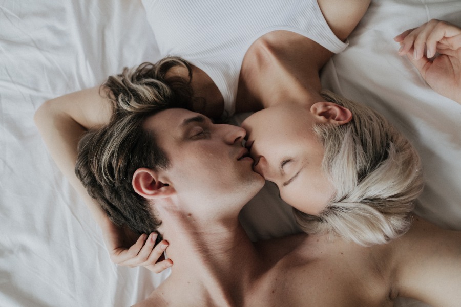 Мъж и жена се целуват в леглото, статия за забавяне на еякулация и удължаване на времетраенето за секса
